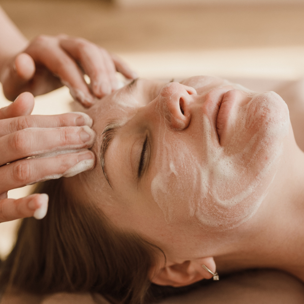 Woman receiving a facial treatment with esthetician using a face cleanser